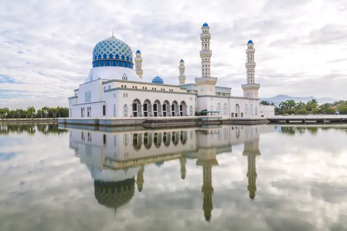 Exterior view of mosque with white washed facade and blue dome reflected in a pond.