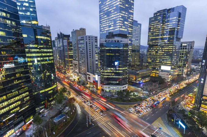 High angle view over city with illuminated skyscrapers, busy street junction and light trails of cars.