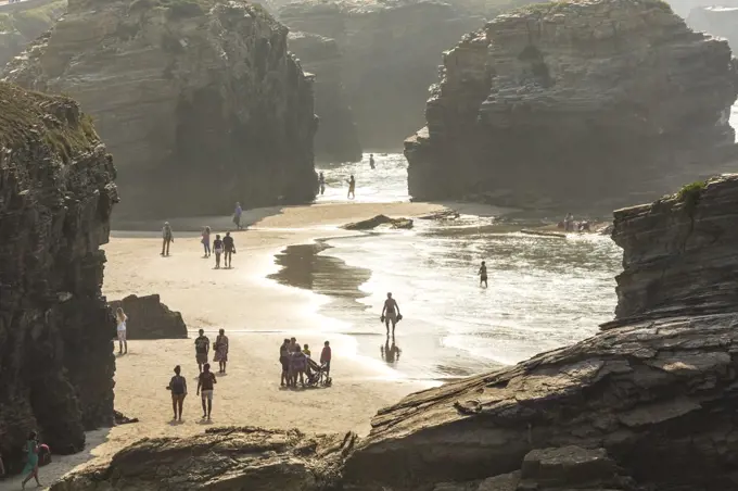 People on sandy beach surrounded by rocks.