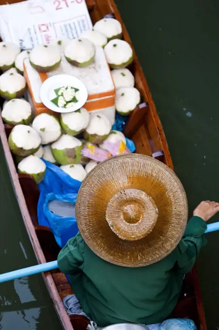 High angle view of person wearing hat sitting in narrow boat, transporting green coconuts.