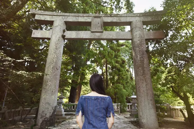 Rear view of young woman wearing blue dress standing at Shinto Sakurai Shrine, Fukuoka, Japan.