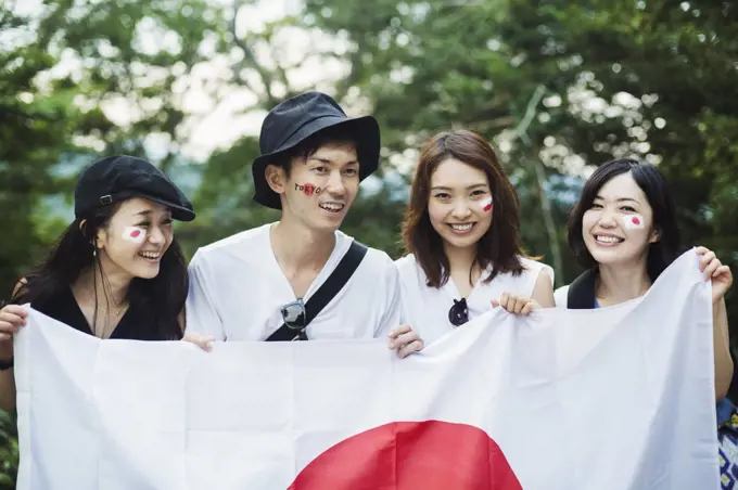 Smiling man and three young women standing outdoors, faces painted, holding Japanese flag.