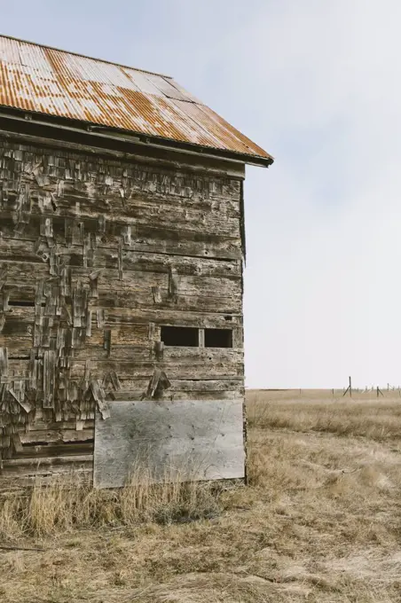 An old abandoned farmhouse with wooden shingle tiles on the walls. Silvery grey colours.