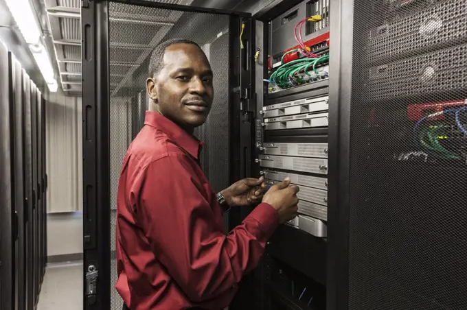 Black man technician working on computer servers in server farm.