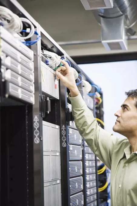 Male computer technician working on servers in a computer server farm.