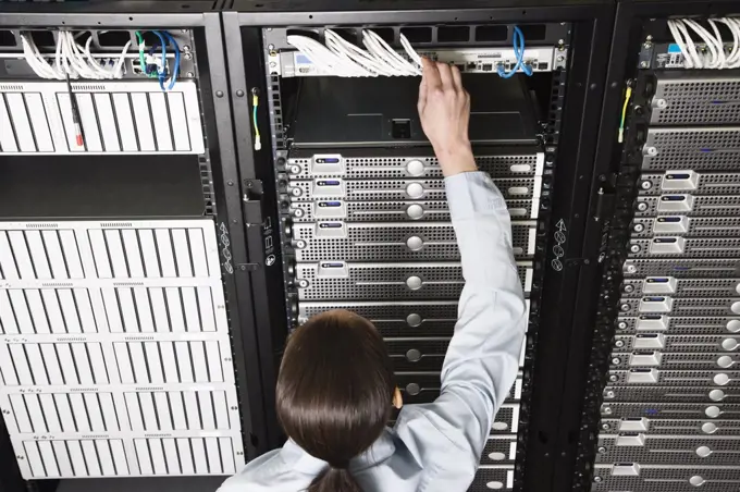 Caucasian woman lab technician working on servers in a computer sever farm.