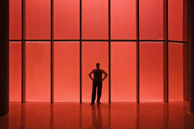 Businessman standing next to red tinted windows in an office lobby.