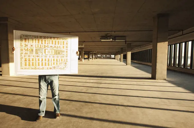 Businessman holding up plans for new office space standing in the middle of the empty raw space.