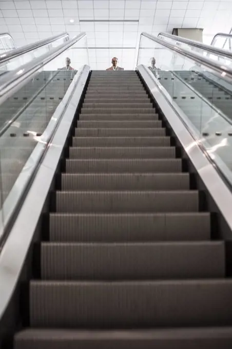 Looking up an escalator with a person about to get on the escalator in a convention center space.