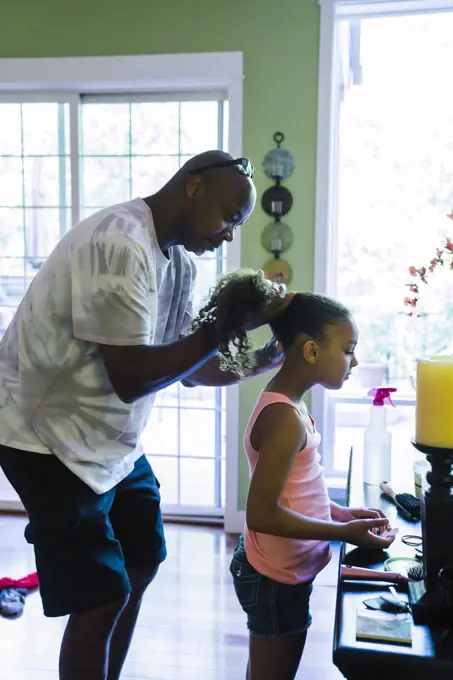 Dad fixing his daughter's hair, holding it and plaiting it.