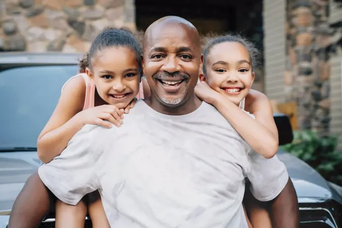 Portrait of happy dad hugging daughters in front of house