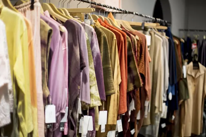 A hanging rail of women's clothing dyed using natural plant dyes, on a rail in a store.
