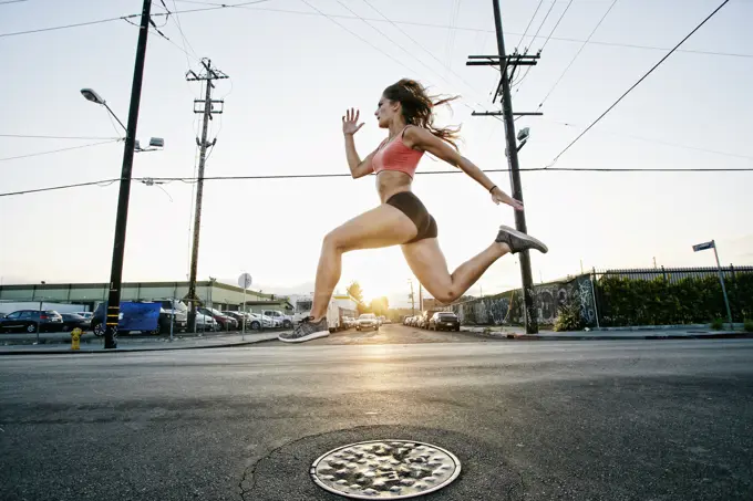 Female athlete running along street at dusk.