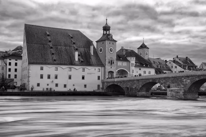 Medieval stone arch bridge over the Danube river with historic buildings and city gate, Regensburg, Germany.