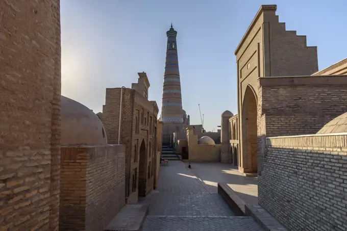 Sunrise, a narrow street of brick buildings and a view of a tall round brick built minaret in Khiva, Uzbekistan.