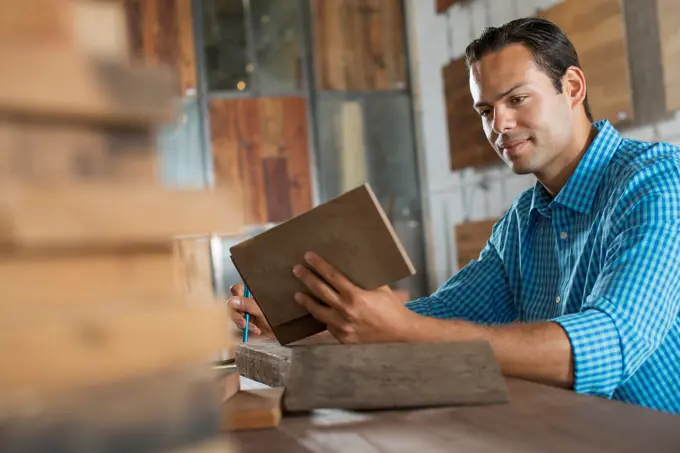 A young man in a workshop which uses recycled and reclaimed lumber to create furniture and objects. Examining a wood sample.