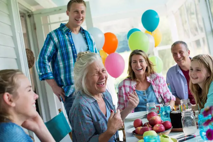 A birthday party in a farmhouse kitchen. A group of adults and children gathered around a chocolate cake.