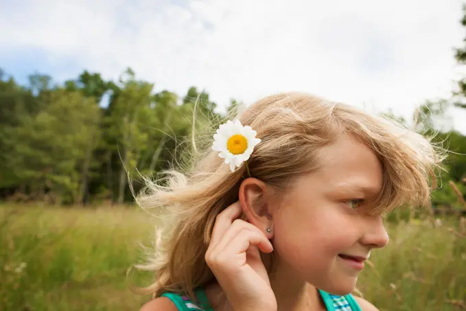 A young girl in the open air, with a daisy like flower behind her ear. New York state, USA. 6/26/2012