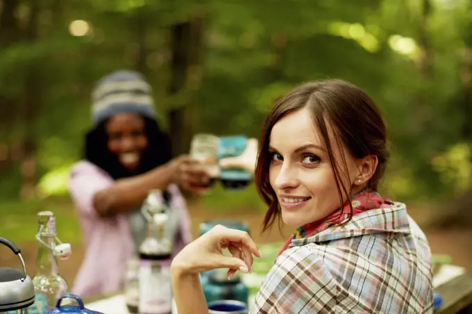 Two young woman drinking a toast at a picnic site or campsite in the woods.  New York State, USA