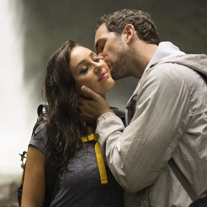 Man kissing cheek of woman near waterfall in jungle