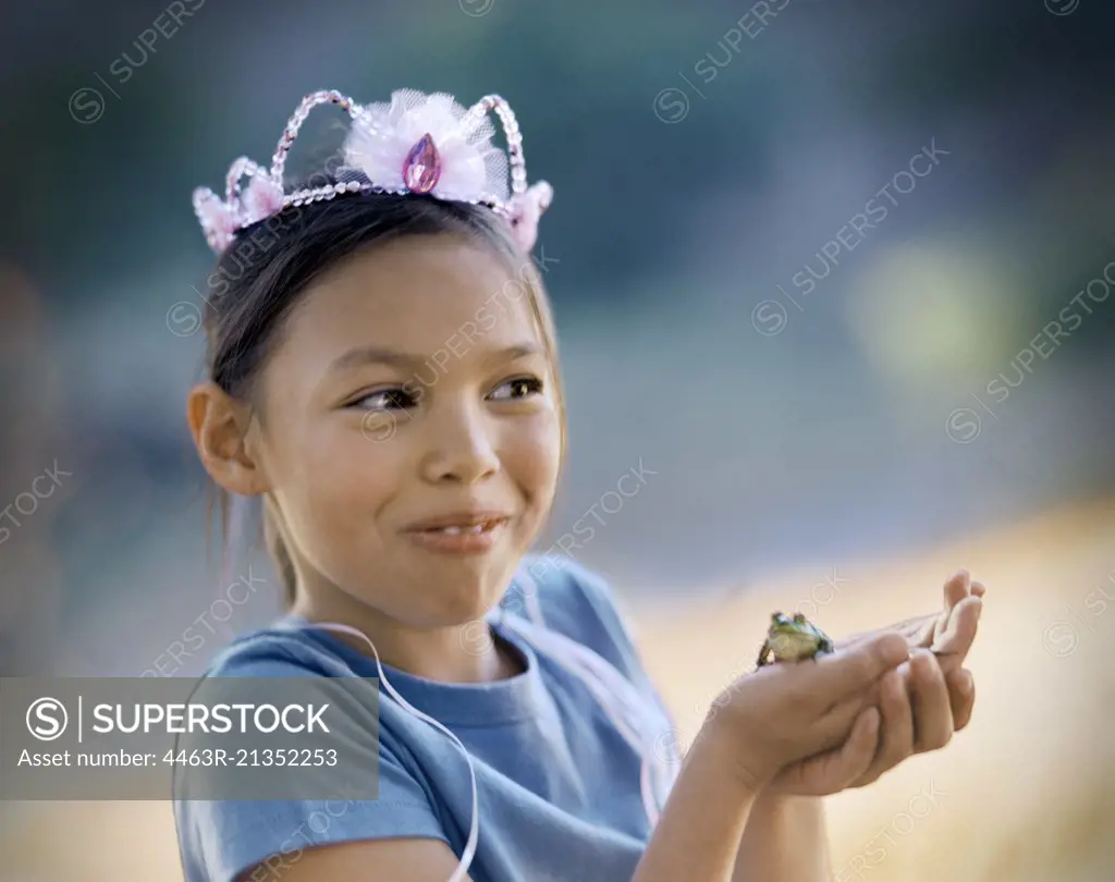 Young girl wearing a crown and holding a green frog in her hands.