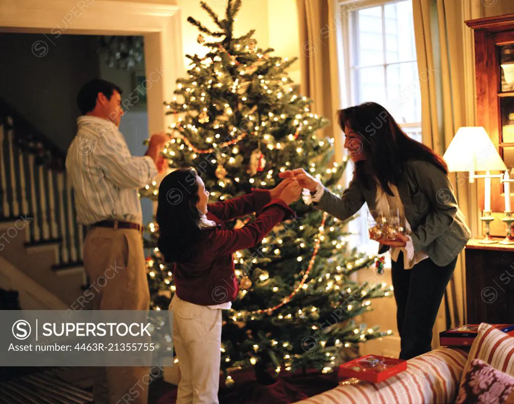 Girl decorating Christmas tree with parents