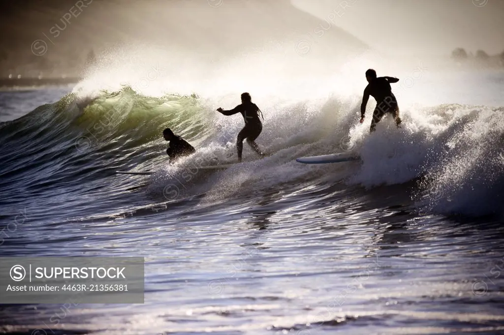 Three people surfboarding on the crest of a wave.