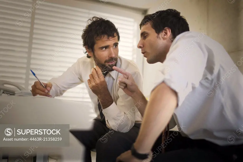 Two businessmen having a discussion at a desk inside an office.