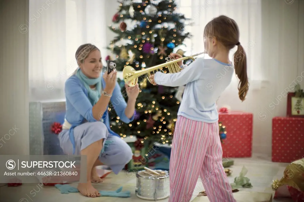 Young girl playing a trumpet while her mother takes a photograph.