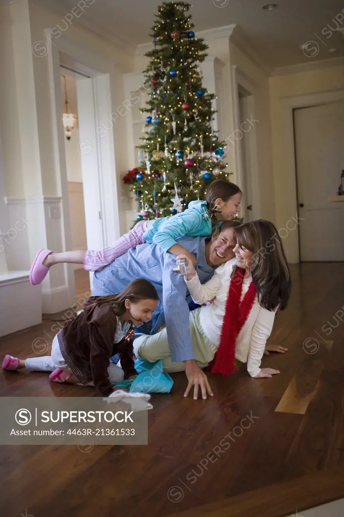 Happy family playing together next to the Christmas tree inside their home.