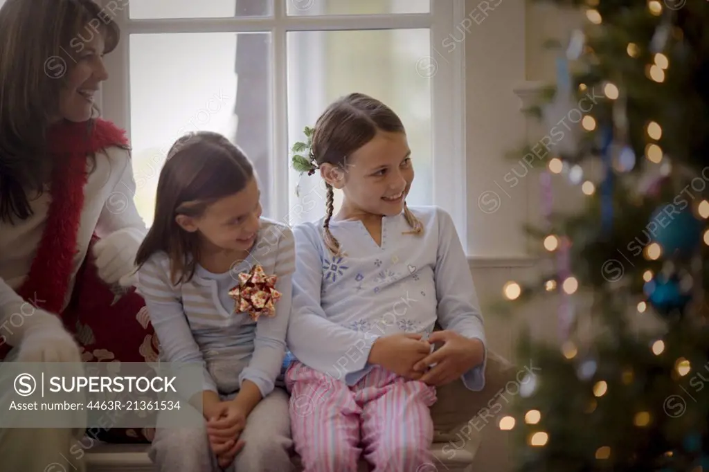 Two smiling young sisters and their mother sitting side by side on Christmas day.