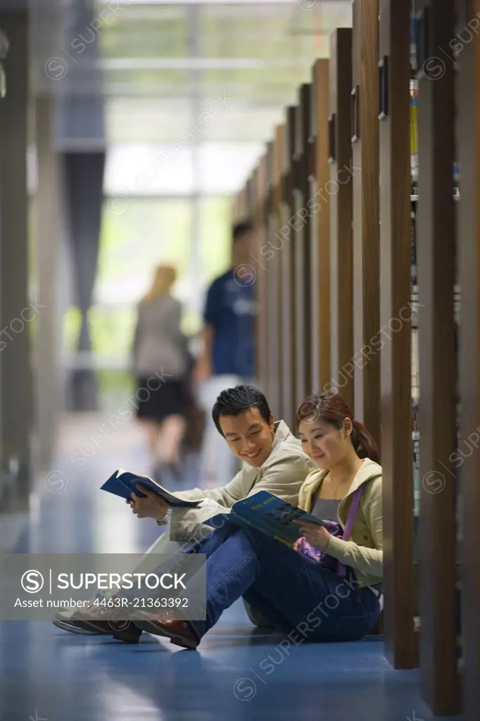 Teenage couple sitting on the floor of a library reading.