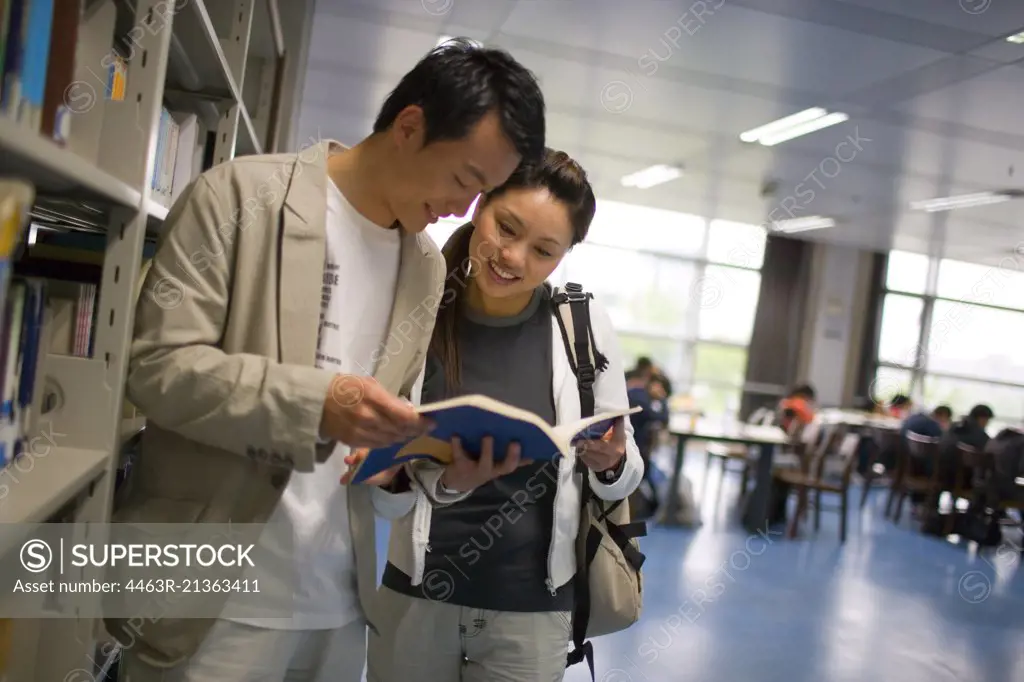 Teenage couple reading a book in a library.