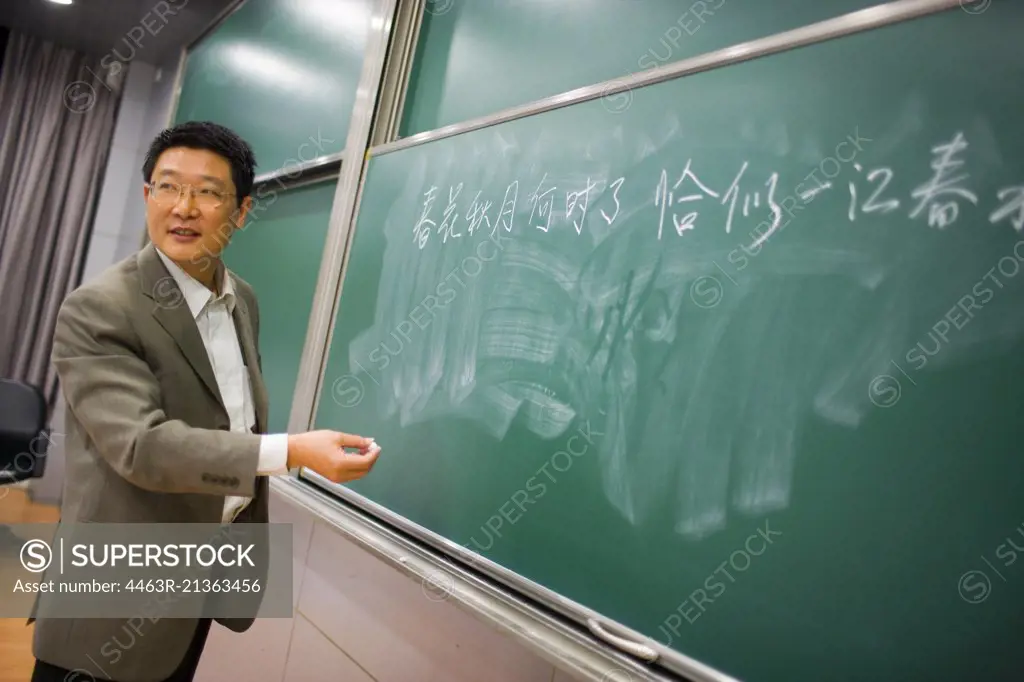 Mid-adult male teacher writing on a chalk board.