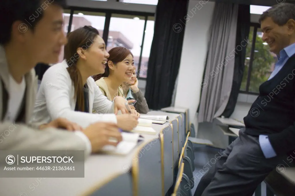 Teenage girls and a boy sitting in a lecture theatre with their mid-adult male teacher.