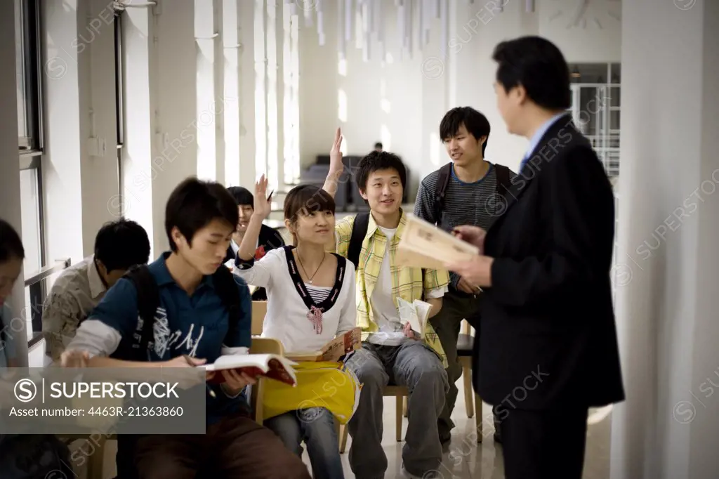 Teenage students talking with their mid-adult teacher in a classroom.