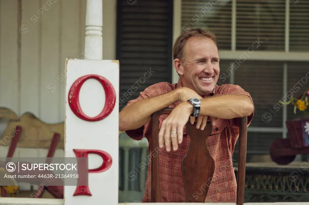 Smiling mature store owner relaxes on the veranda of his antiques shop.