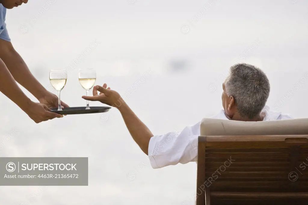 Beach resort waiter serving wine to man on lounger