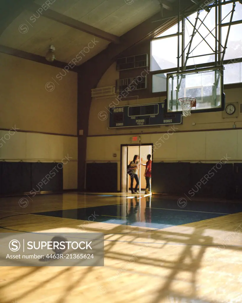 Teenage boy and girl talking in the doorway of a school gymnasium.