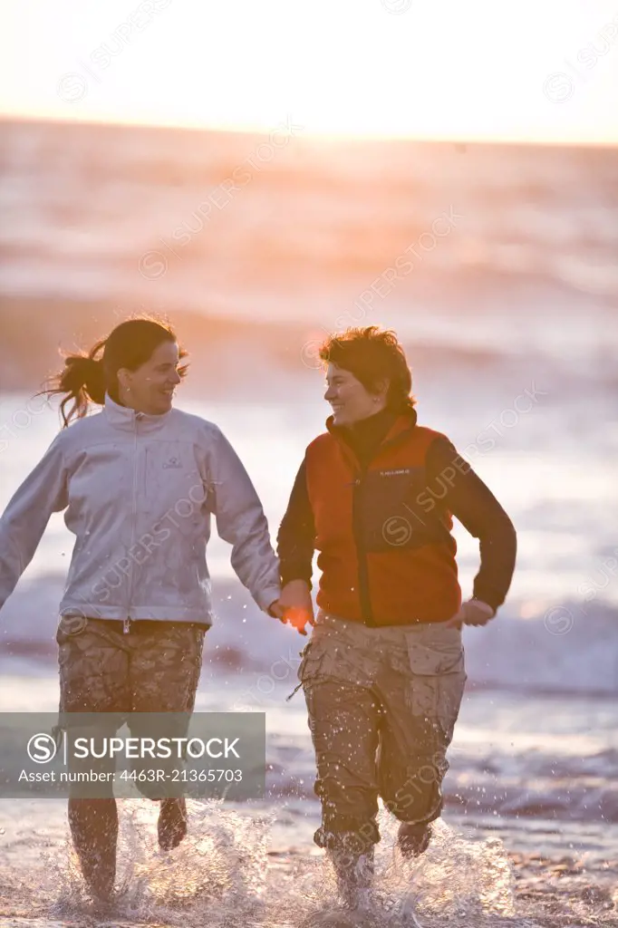 Two women holding hands while running on a beach.