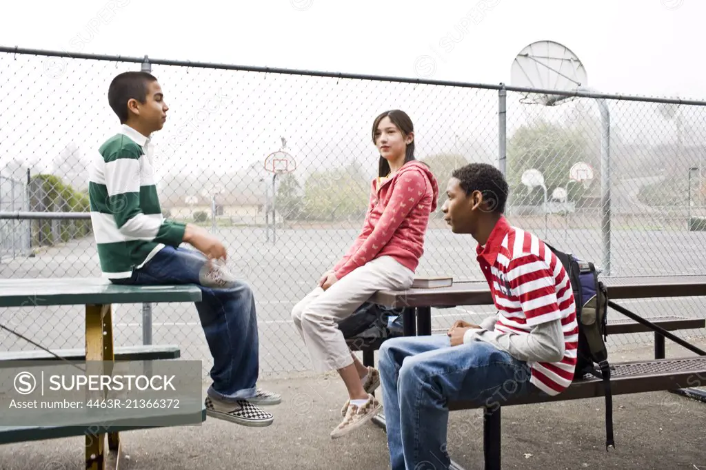 Three teenagers sitting together next to a basketball court.