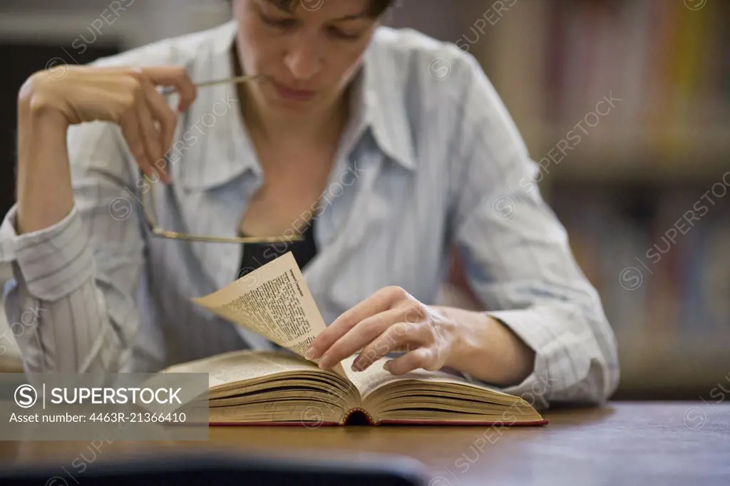 Focused mid adult woman reading a book in a library.