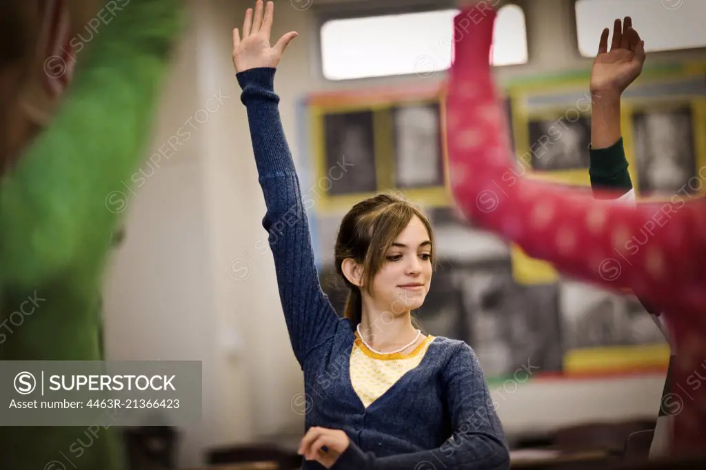 Teenage girl raising her hand in a classroom with other students.