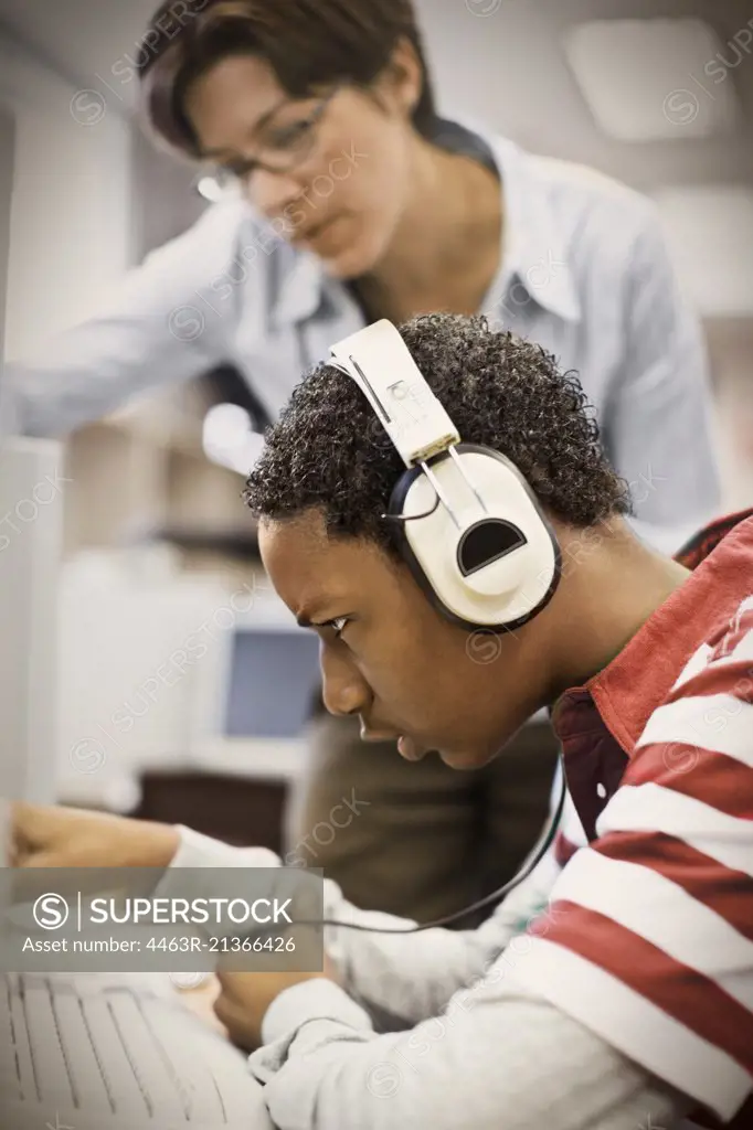 Student using computer while his teacher watches