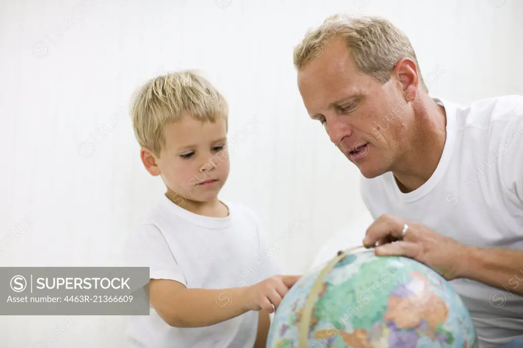 Mid-adult man sitting with his young son looking at a globe.