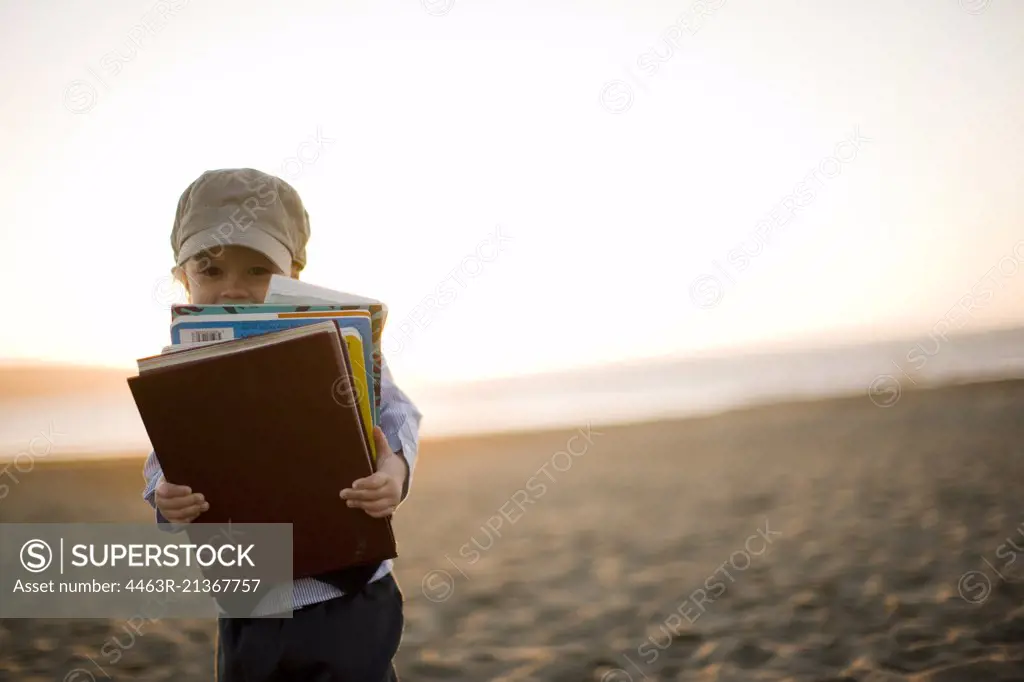 Little boy in old-fashioned clothing carrying books on the beach