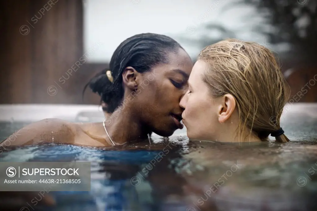 Young lesbian couple kissing while sitting in a hot tub.
