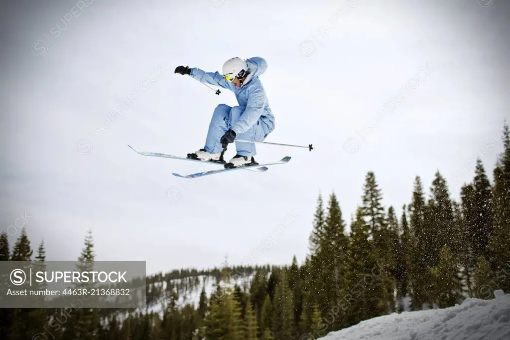 Young man jumping mid-air while riding his skis outdoors in the snow.