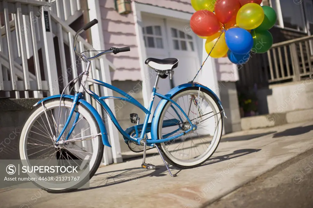 Blue bicycle with bunch of colorful balloons tied to it.