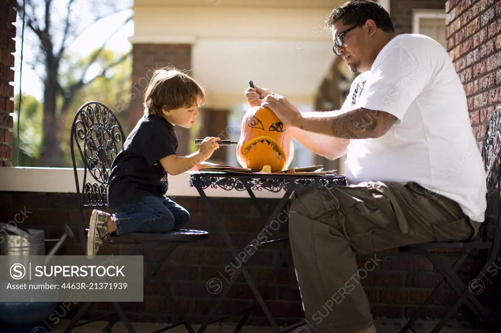 Father and son drawing face on pumpkin and carving Jack O' Lantern